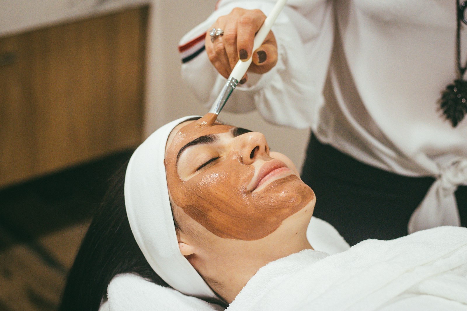 An aesthetician applying a warm clay mask during a facial at Lueur